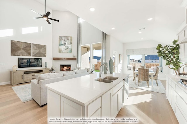 kitchen featuring white cabinets, light wood-style flooring, open floor plan, a lit fireplace, and a sink