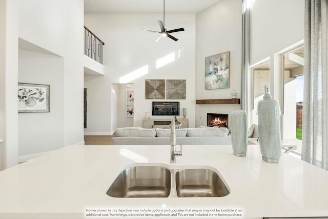 kitchen with a towering ceiling, a ceiling fan, open floor plan, a lit fireplace, and light countertops