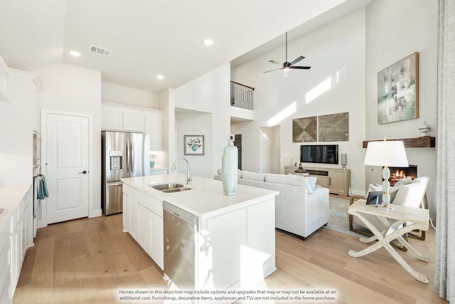 kitchen with a warm lit fireplace, visible vents, light wood-style flooring, appliances with stainless steel finishes, and a sink