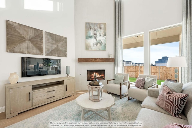 living area with a towering ceiling, light wood finished floors, and a tile fireplace