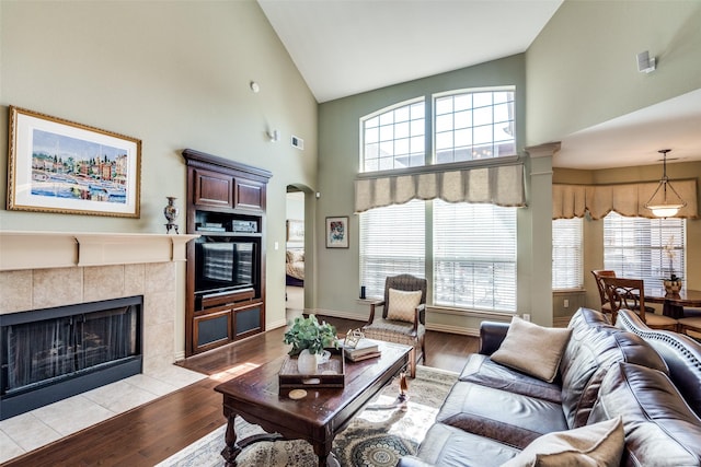 living area featuring light wood-style floors, arched walkways, high vaulted ceiling, and a tile fireplace