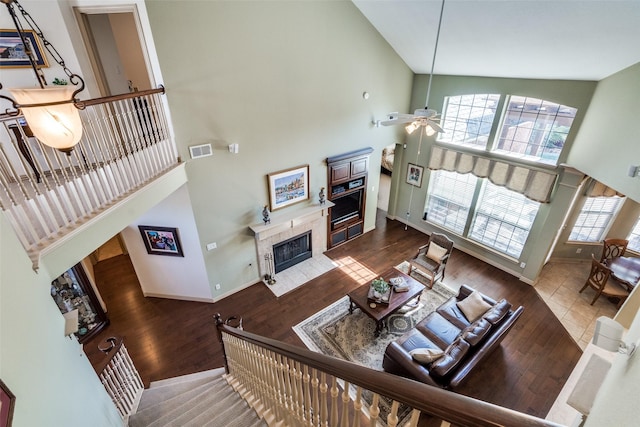 living area featuring visible vents, a tiled fireplace, a towering ceiling, ceiling fan, and wood finished floors