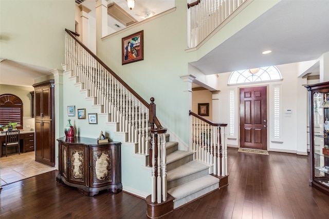 foyer entrance with stairs, a towering ceiling, baseboards, and hardwood / wood-style flooring