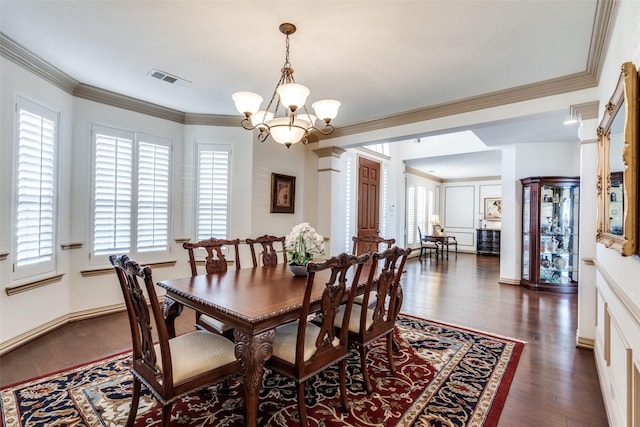 dining room featuring a notable chandelier, crown molding, dark wood-type flooring, visible vents, and ornate columns