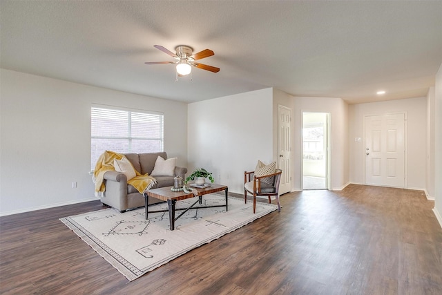 living area with a textured ceiling, dark wood-style flooring, a ceiling fan, and baseboards