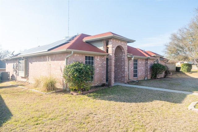 view of front of property with central air condition unit, a front lawn, solar panels, and brick siding