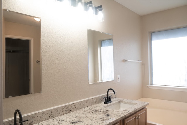 bathroom with a textured wall, vanity, and a bath