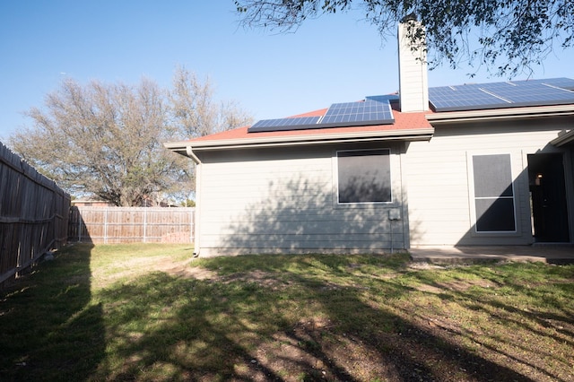 rear view of property featuring a fenced backyard, a chimney, solar panels, and a yard