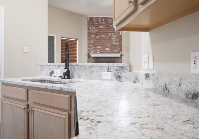 kitchen with light brown cabinets, a sink, and light stone countertops