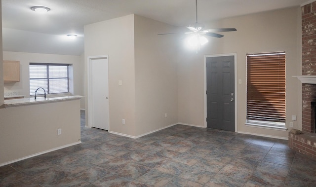 unfurnished living room featuring ceiling fan, a fireplace, a sink, and baseboards