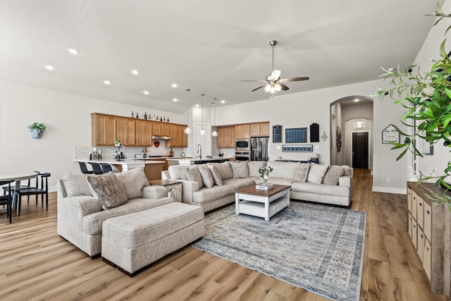 living area with a ceiling fan, arched walkways, light wood finished floors, and recessed lighting