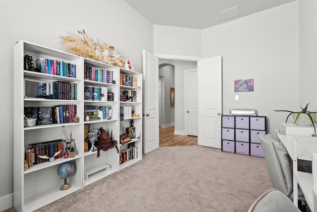 carpeted home office featuring arched walkways and visible vents