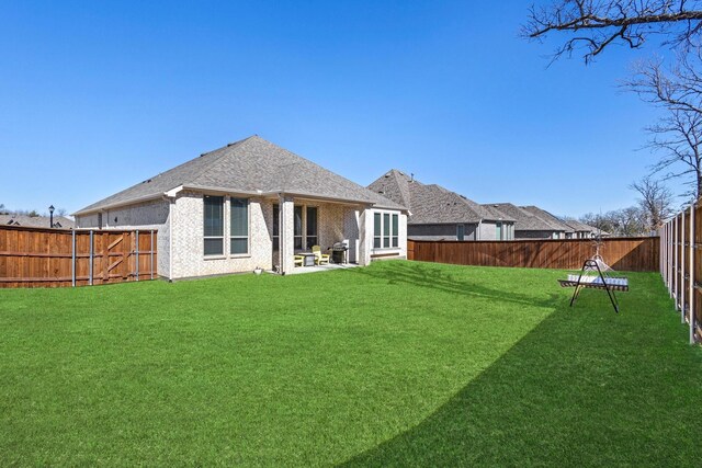 back of house with a patio, a fenced backyard, brick siding, a yard, and roof with shingles