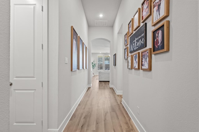 hallway featuring arched walkways, baseboards, visible vents, and light wood finished floors