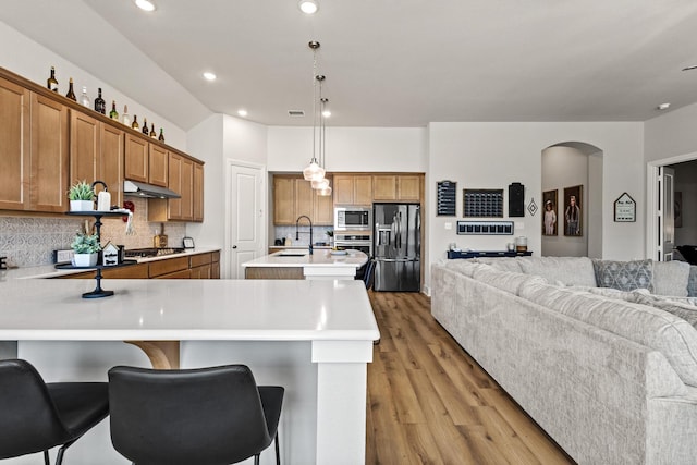 kitchen with brown cabinets, open floor plan, stainless steel appliances, under cabinet range hood, and a sink