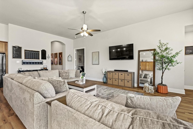 living room featuring arched walkways, ceiling fan, wood finished floors, and baseboards