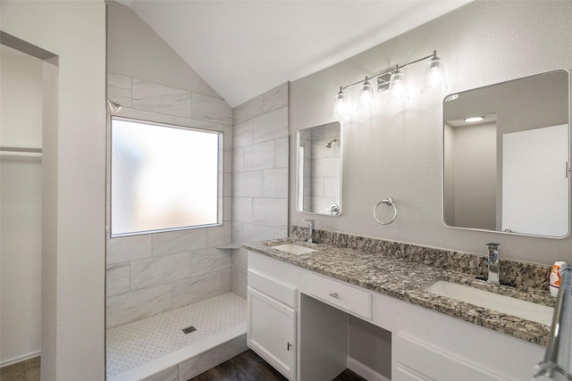 bathroom with vaulted ceiling, a sink, a tile shower, and double vanity