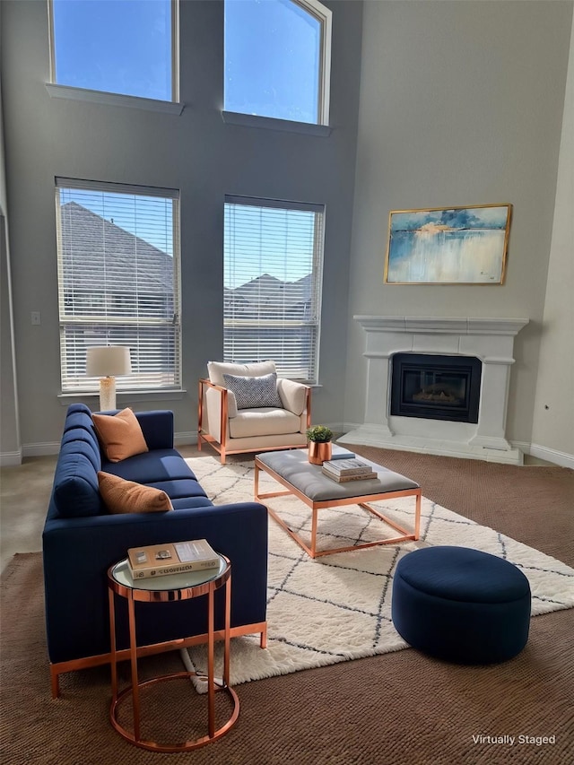 living room featuring a premium fireplace, carpet flooring, a towering ceiling, and baseboards