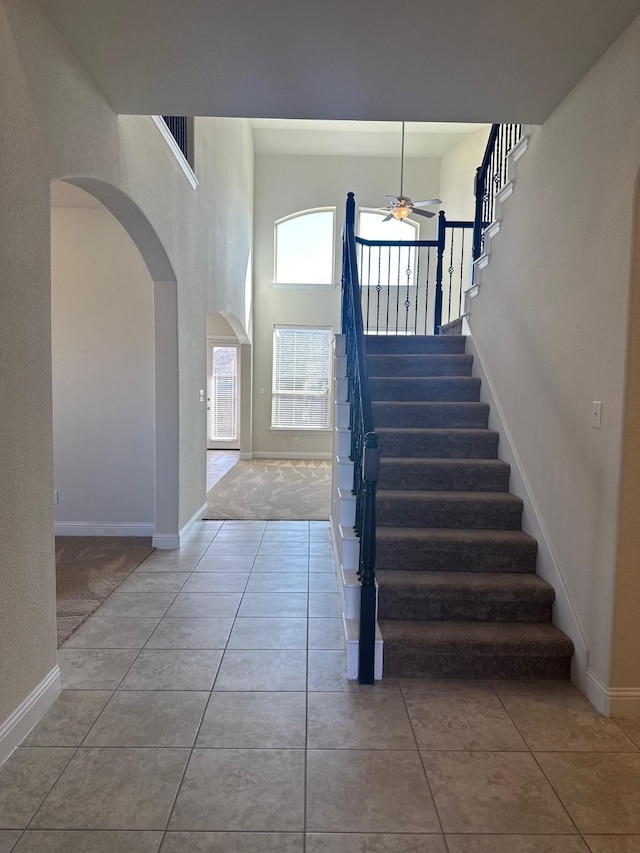 tiled foyer entrance with arched walkways, stairs, a ceiling fan, and baseboards