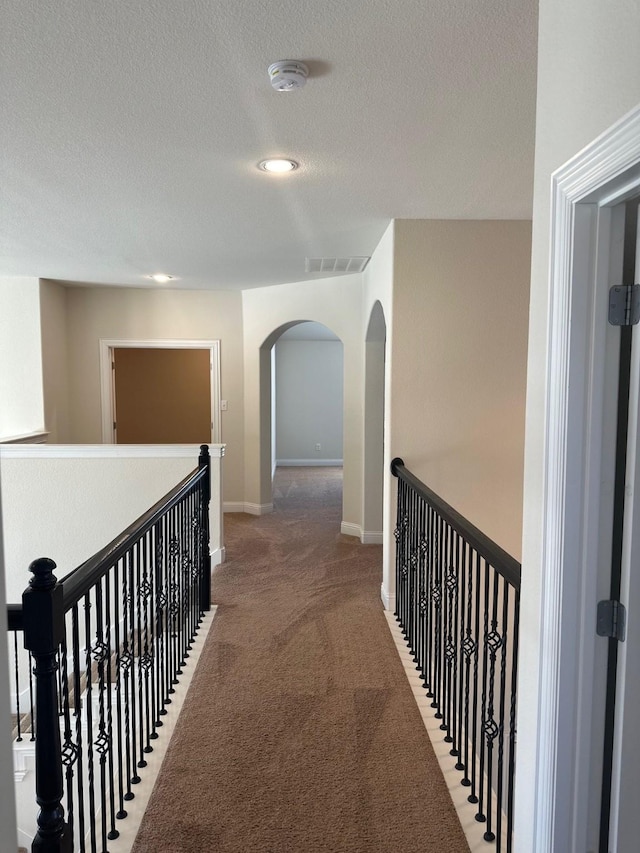 corridor with visible vents, arched walkways, carpet, a textured ceiling, and an upstairs landing