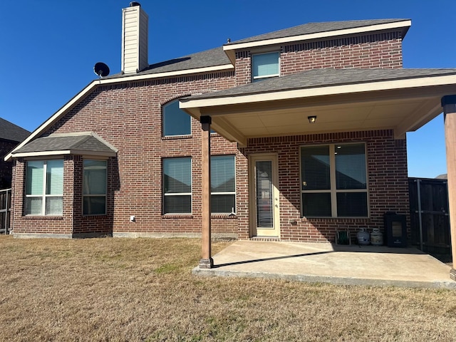 back of house featuring brick siding, a patio, a chimney, and a lawn