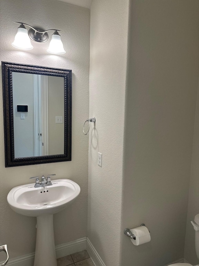 half bathroom with toilet, baseboards, and tile patterned floors