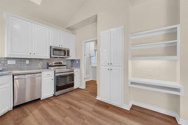 kitchen featuring appliances with stainless steel finishes, vaulted ceiling, light wood-style floors, white cabinetry, and backsplash