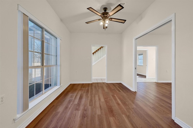 spare room featuring visible vents, baseboards, a ceiling fan, wood finished floors, and stairs