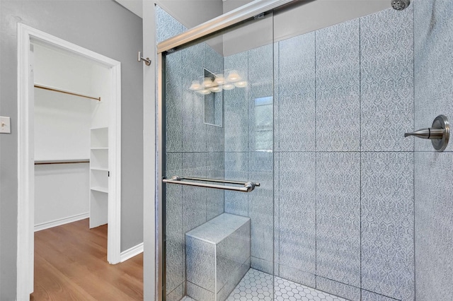 bathroom with a shower stall, a spacious closet, baseboards, and wood finished floors