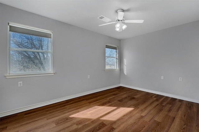 empty room featuring a ceiling fan, visible vents, baseboards, and wood finished floors