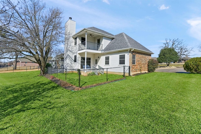 rear view of house featuring a balcony, a fenced front yard, ceiling fan, and a yard