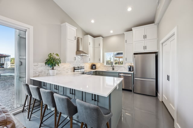 kitchen featuring a peninsula, wall chimney range hood, stainless steel appliances, and backsplash