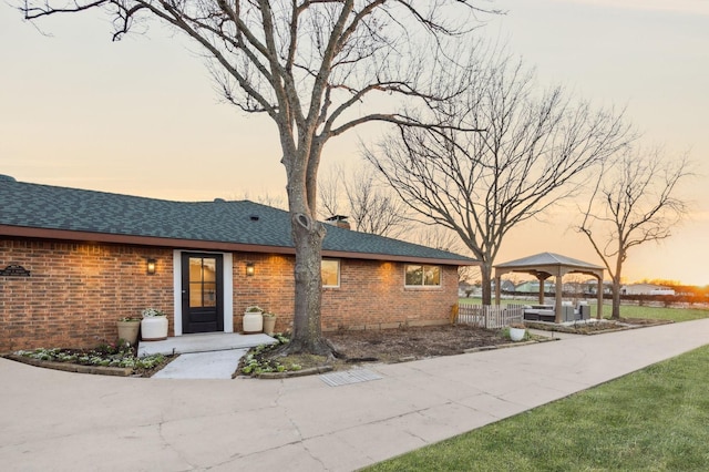 single story home with brick siding, a chimney, a gazebo, and roof with shingles