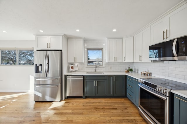 kitchen with decorative backsplash, appliances with stainless steel finishes, light wood-style floors, white cabinetry, and a sink