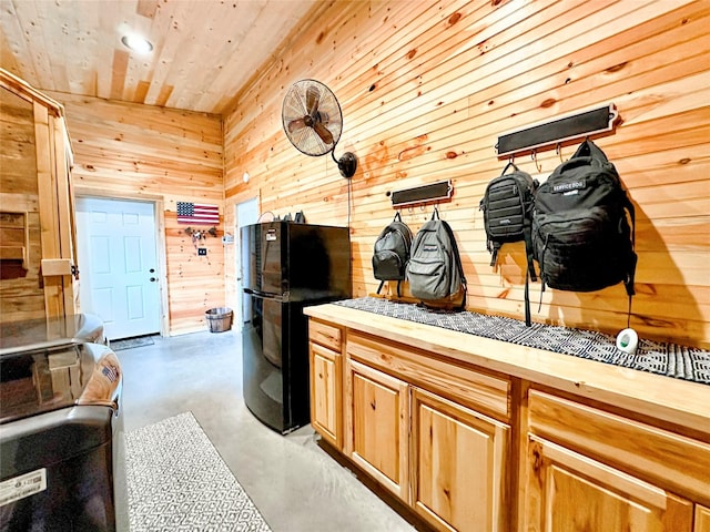 kitchen featuring washer / dryer, wooden counters, freestanding refrigerator, wooden walls, and concrete flooring