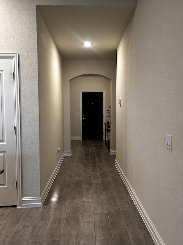 hall with dark wood-style floors, baseboards, and arched walkways