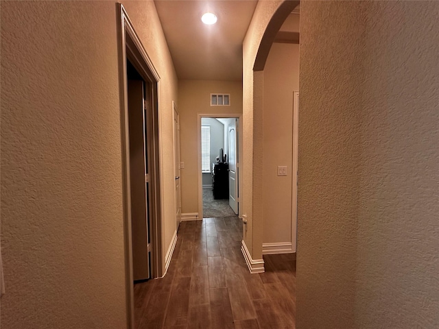 hallway featuring arched walkways, a textured wall, dark wood-style floors, and visible vents