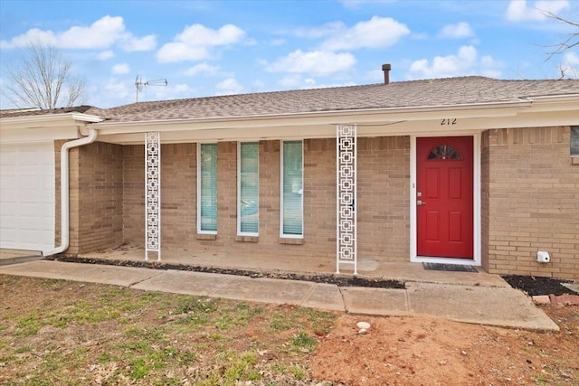 doorway to property with a garage, brick siding, and a shingled roof