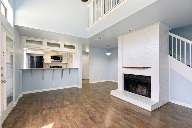 unfurnished living room with a high ceiling, a brick fireplace, baseboards, and dark wood-style flooring