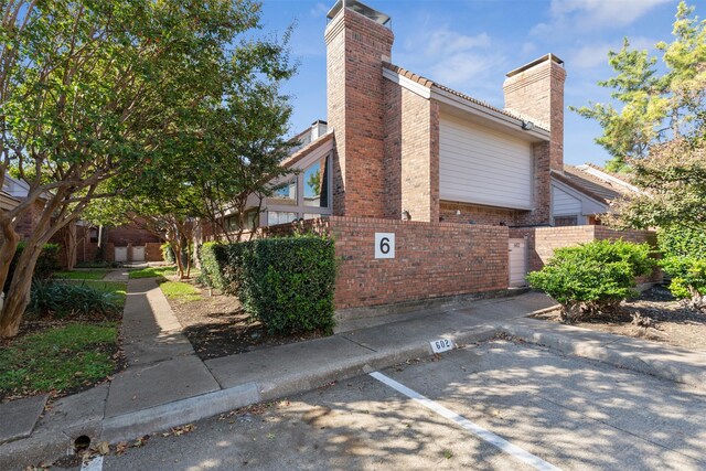 view of side of home with a chimney, fence, and brick siding