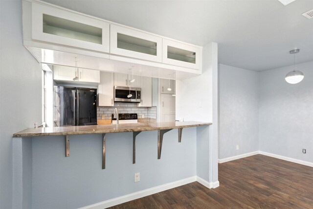 kitchen featuring stainless steel microwave, light stone counters, a breakfast bar area, backsplash, and freestanding refrigerator