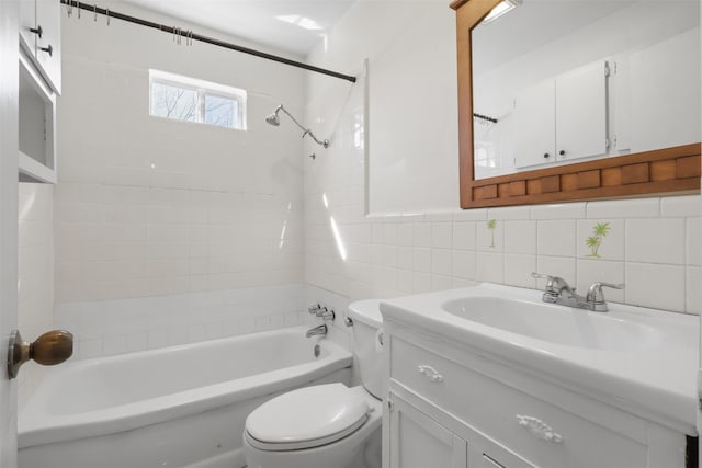 full bath with tile walls, bathing tub / shower combination, toilet, wainscoting, and vanity