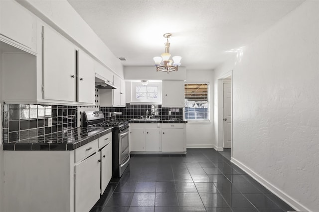 kitchen with tile counters, decorative backsplash, white cabinetry, under cabinet range hood, and stainless steel gas range oven