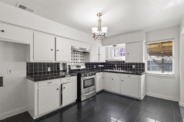 kitchen featuring tile counters, visible vents, gas stove, white cabinets, and under cabinet range hood