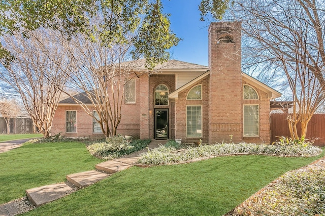 view of front of property with brick siding, a chimney, a front yard, and fence