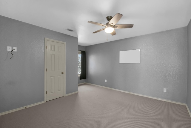 carpeted spare room featuring ceiling fan, visible vents, baseboards, and a textured wall