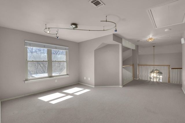 carpeted spare room featuring baseboards, attic access, visible vents, and track lighting