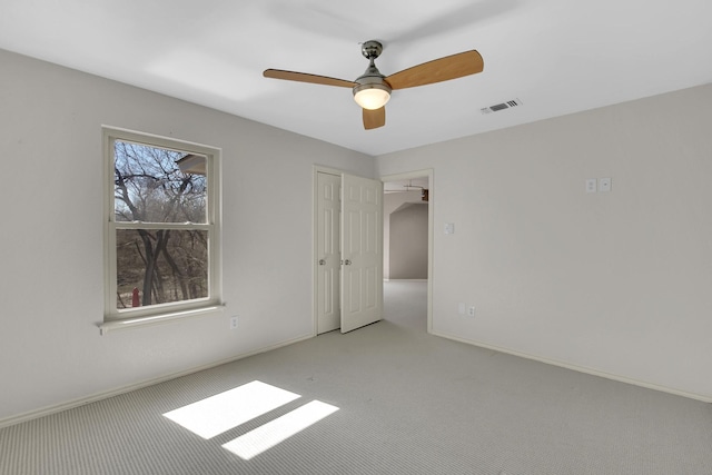 empty room with carpet floors, visible vents, baseboards, and a ceiling fan