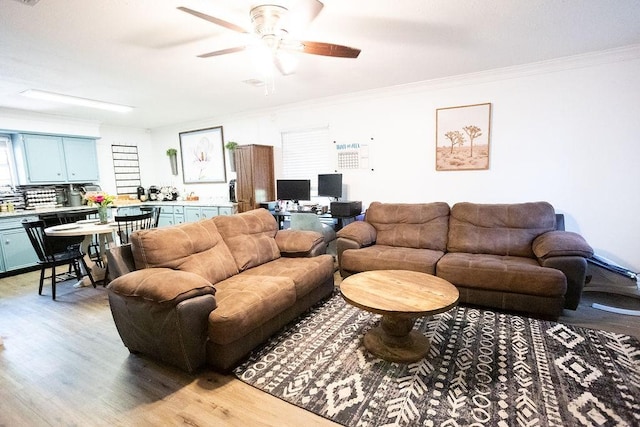 living area featuring crown molding, light wood-style flooring, and ceiling fan