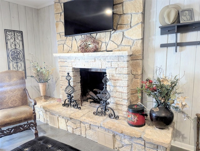 living room featuring a stone fireplace, wood finished floors, visible vents, and crown molding